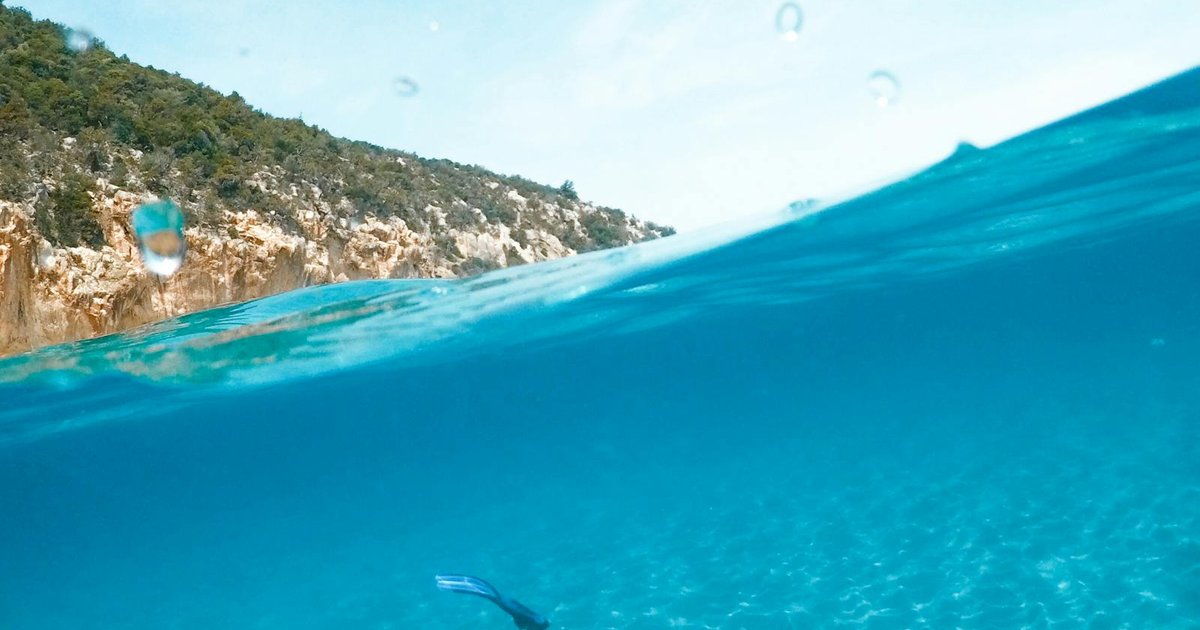 Snorkeler swimming in crystal-clear turquoise water above rocks in Corfu
